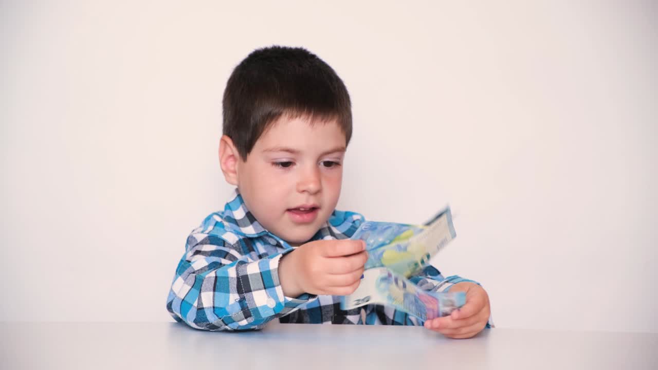 A 4-year-old boy counts money, holds euros in his hands.