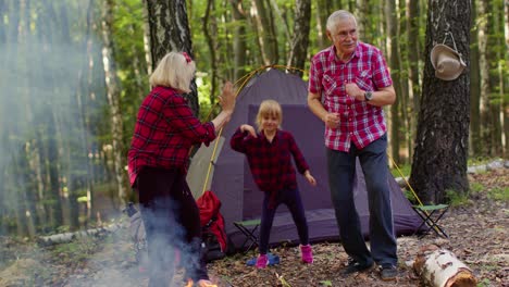 Ältere-Großmutter-Und-Großvater-Mit-Enkelin-Tanzen-Und-Feiern-Am-Lagerfeuer-Im-Wald.