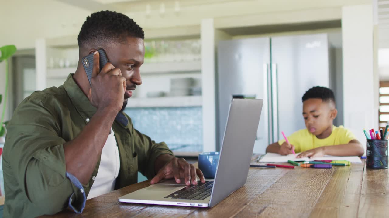Afrikaans-Amerikaanse vader en zoon maken huiswerk, praten aan de telefoon en gebruiken samen een laptop.