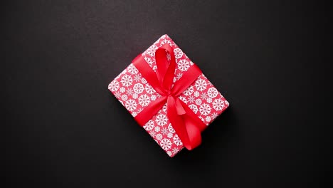 Red-gift-box-with-red-bow-on-black-table--top-view