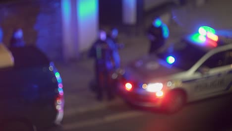 faro de policía parpadeante en coche de policía y grupo de oficiales alrededor, vista nocturna borrosa