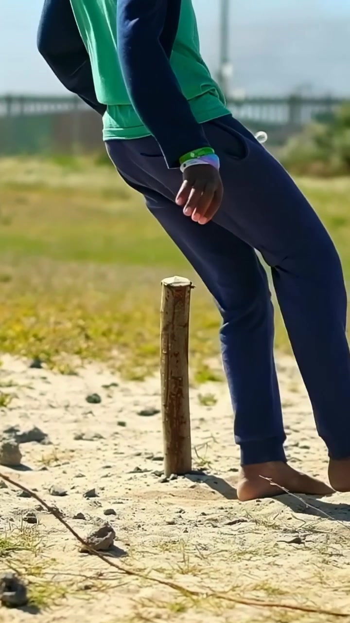 Video vertical: Adolescente descalzo con camiseta verde bajando de un escalón y pateando un balón para jugar en la arena, con espacio para texto.