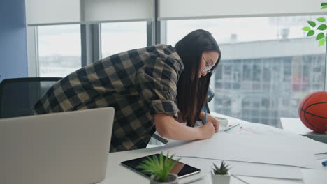 Eyeglasses-architect-drawing-blueprints-at-windows-workplace.-Woman-writing-plan