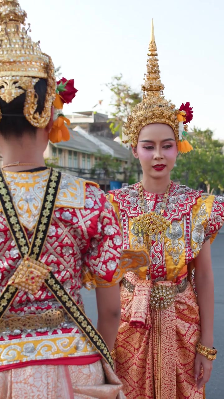 Dua penari Thailand dengan kostum emas berornamen menyesuaikan hiasan kepala di luar ruangan saat siang hari yang cerah
