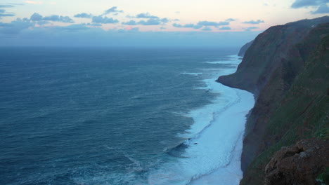 serene ocean view at sunset steep cliff covered in green vegetation in madeira overlooks the calm sea, waves stretching towards the horizon sky soft clouds and fading sunlight