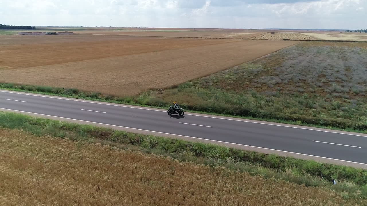 Aerial arc shot of an adrenaline seeking superbike rider, cruising along an open road surrounded by remote farmland, Spain, Europe