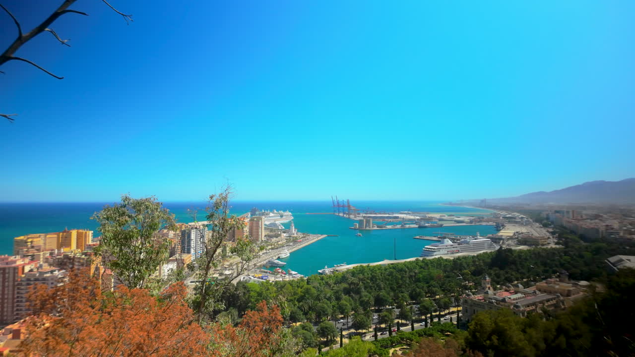 Aerial view of Málaga port and coastline from Gibralfaro, showcasing the harbor, cruise ships, and urban landscape under a bright blue sky