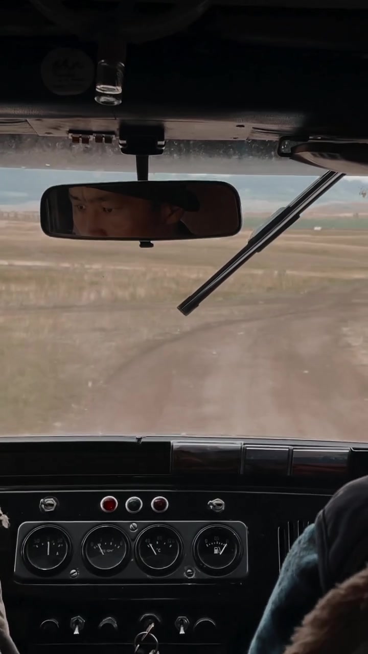 Prospettiva dall'interno di un'auto d'epoca che percorre una strada sterrata rurale attraverso un paesaggio di steppa aperta nei Monti Altai, Russia, con cruscotto e specchietto retrovisore visibili