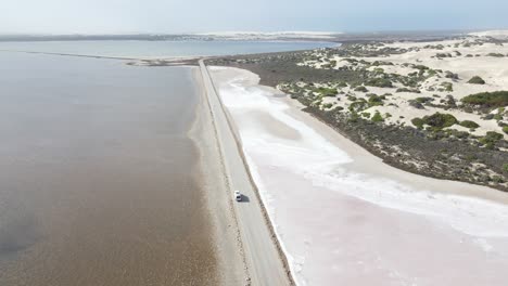 Avión-Teledirigido-Sobre-Una-Autocaravana-Blanca-Conduciendo-Por-Una-Carretera-Sobre-El-Lago-Rosa-Macdonnell-Y-Dunas-De-Arena-En-El-Sur-De-Australia