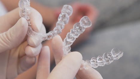 tight close-up of orthodontist putting two invisalign aligners side by side, with patient in the background