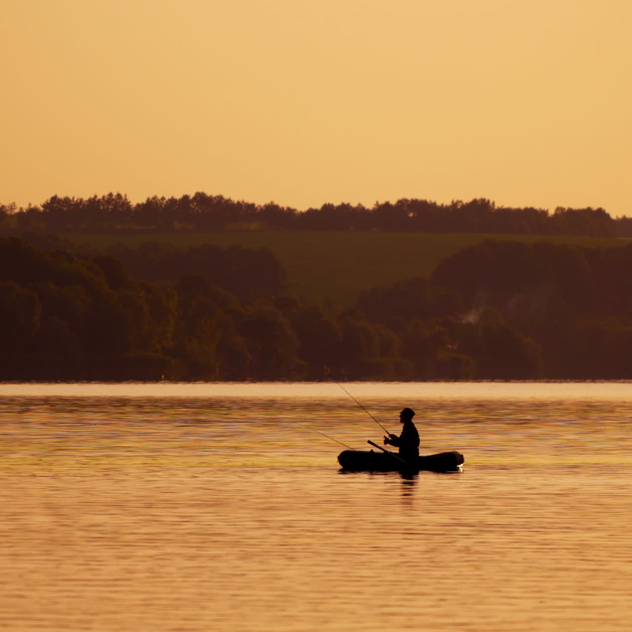 Silhouette of a man with fishing rods in the middle of the lake at sunset. Natural river background in the evening and a fisherman in a boat.