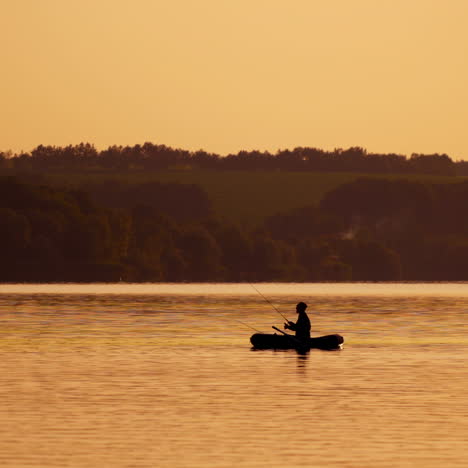 silhouette of a man with fishing rods in the middle of the lake at sunset. natural river background in the evening and a fisherman in a boat.
