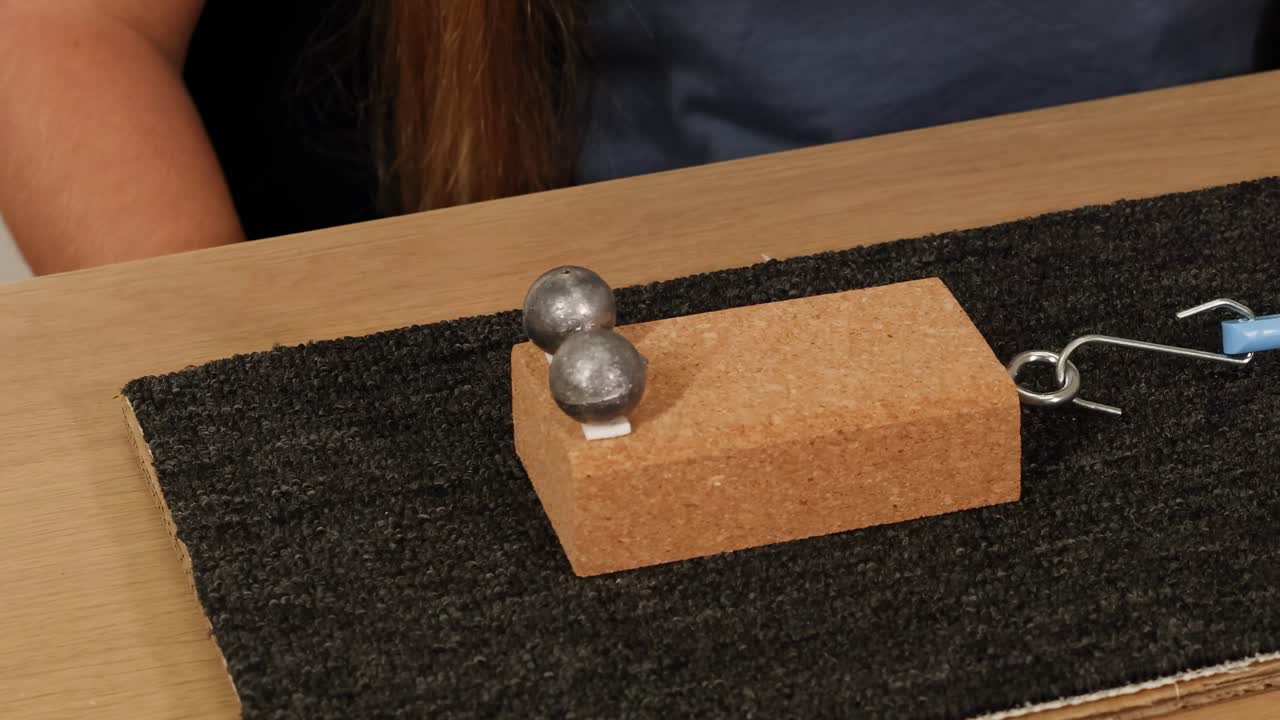 A person demonstrates friction using a cork block, weights, and a textured mat.