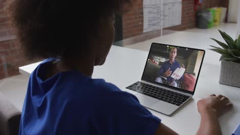 back view of african american woman having a video call with male colleague on laptop at office