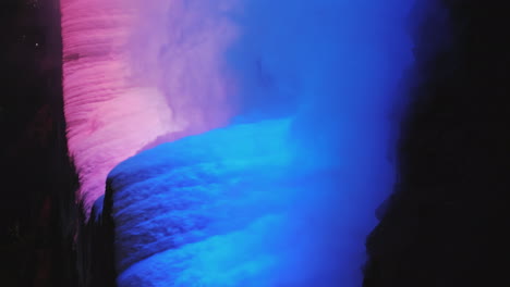 vertical 4k video - night view of niagara falls water streams lit by a blue floodlight