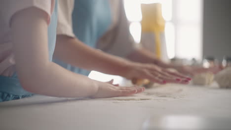 cocinar comida en casa niña pequeña y mujer están rodando la masa en la mesa de la cocina vista de cerca