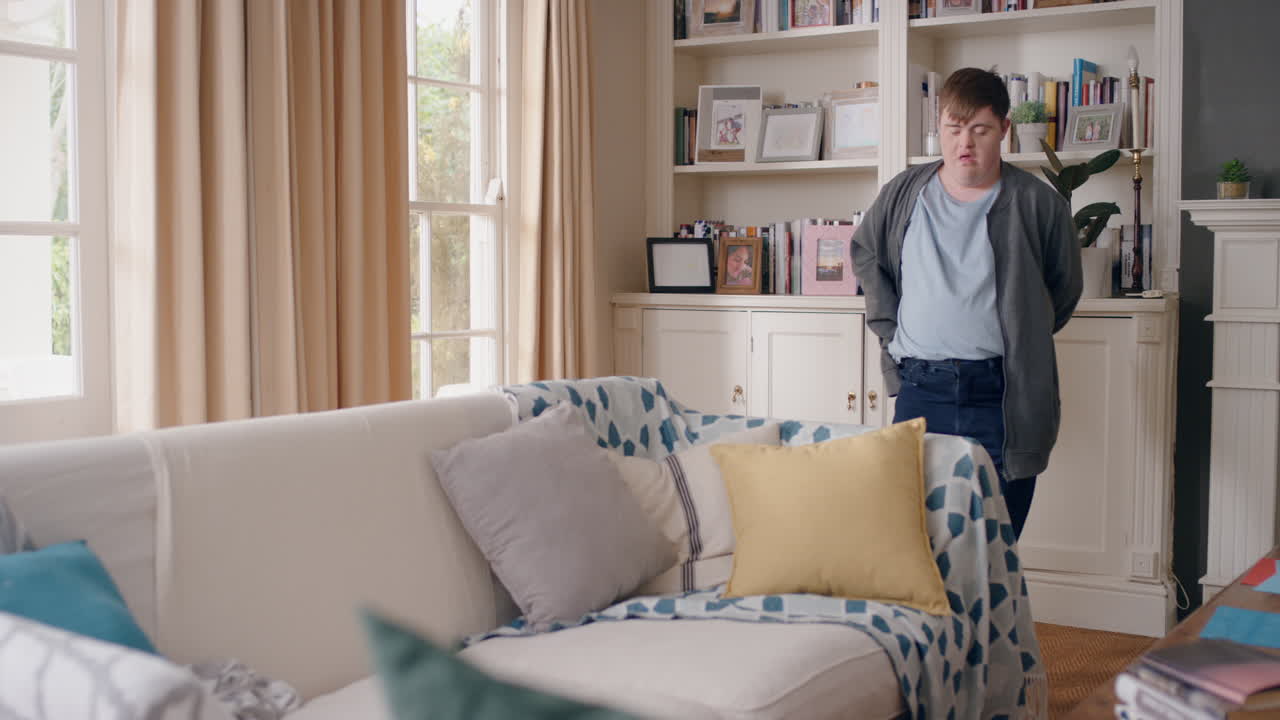 다운 증후군을 가진 재미있는 십대 소년이 거실에서 춤을 추고 재미있게 춤을 추고 어리석은 춤 움직임으로 축하하고 행복한 아이가 집에서 주말을 즐기고 있습니다.