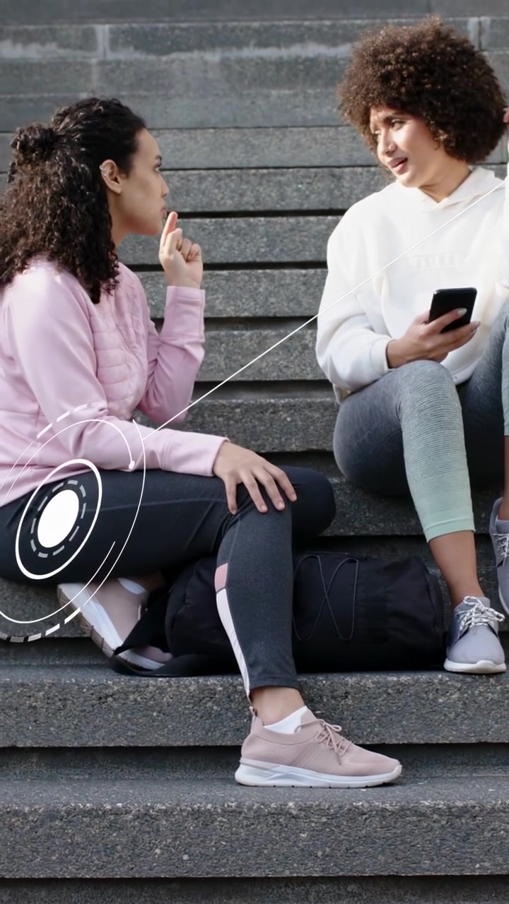 Vertikální video: Žena vlevo gestikuluje, žena vpravo klepe na telefon, což způsobuje překryvy zobrazující marketing.