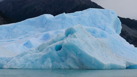 glaciar azul rodeado por una gran montaña asombrosa en el fondo y un cielo gris y triste