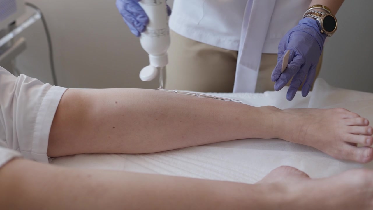 Terapista guantato che applica gel lungo la gamba di un cliente prima di una sessione di epilazione laser.