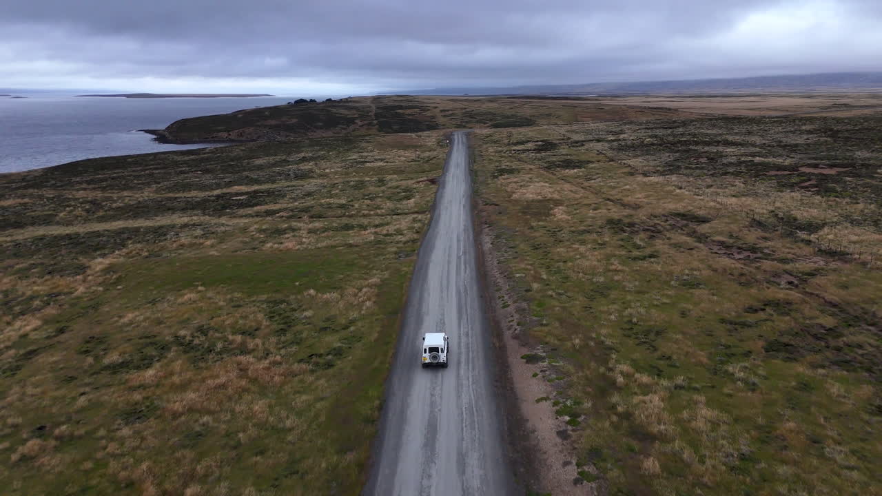 Ripresa rotante con drone di un veicolo lungo il terreno costiero con sfondo oceanico nelle Isole Falkland, ampio filmato aereo