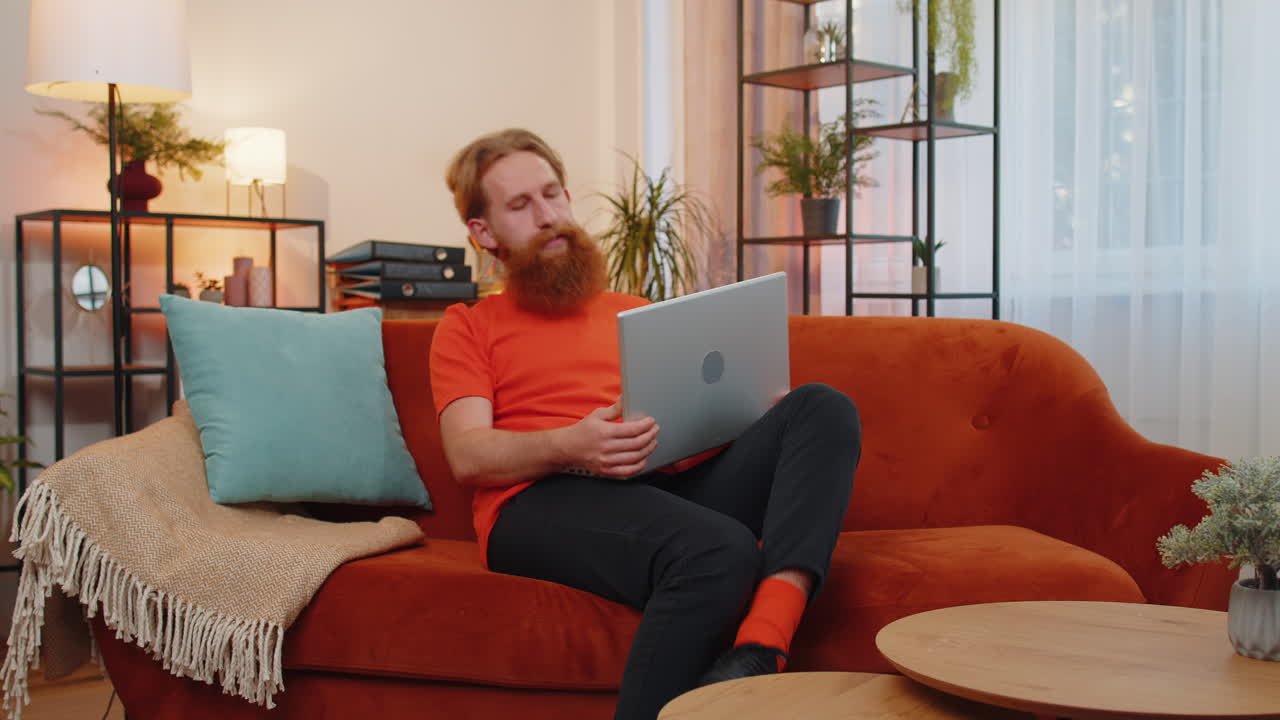 Young man freelancer starts working on laptop pc, sends messages, makes online purchases at home