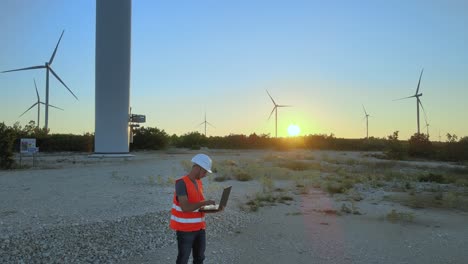 mechanical engineer adjusting wind turbine settings from his laptop during sunset