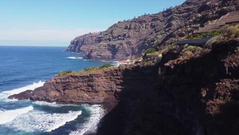 Beautiful-coastline-scenery-blue-ocean-waves-with-green-palm-trees-on-high-cliff-on-Tenerife-on-sunny-day,-flying