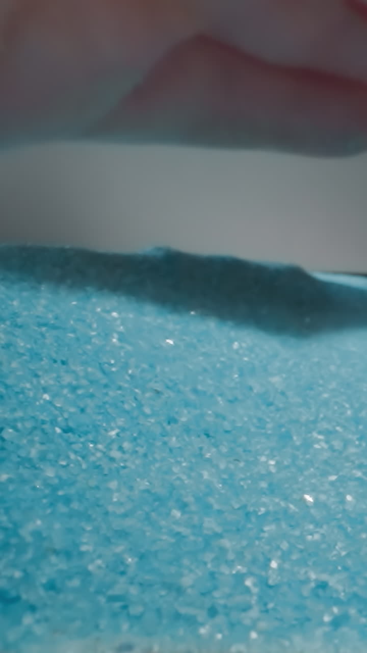 Man shovels light blue sand on plate with hand making heap on grey background. Tiny sandy grains glittering at bright studio light macro slow motion