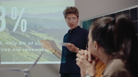 young female engineer explaining presentation about energy efficient architecture on projection screen and talking to colleagues on office meeting, working in green energy company