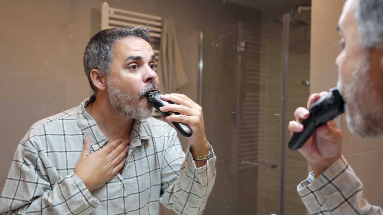 Man Trimming His Beard with an Electric Shaver in the Bathroom Mirror