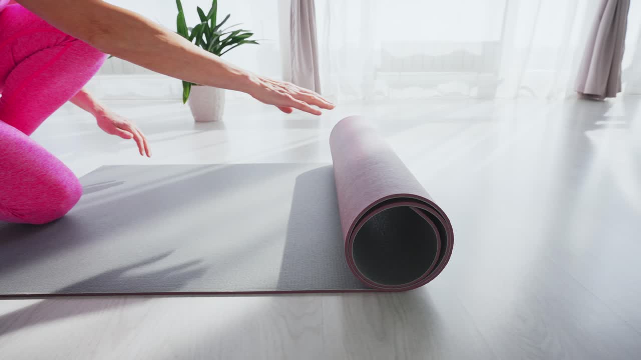 Person som ruller ut yogamatte på tregulv i lyst rom.