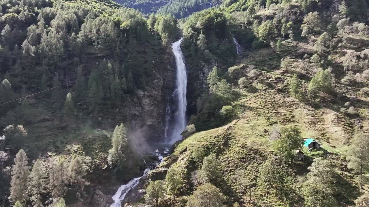 Ripresa aerea circolare di un'alta cascata tra montagne coperte da rocce e alberi, Cascata la Froda