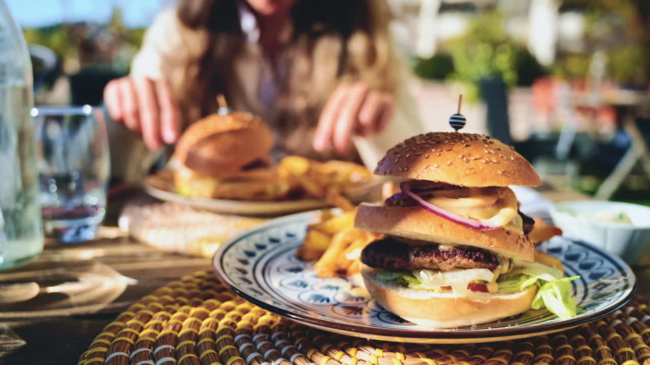 Gourmet burger served on a patterned plate in bright daylight, with blurred restaurant terrace in the background