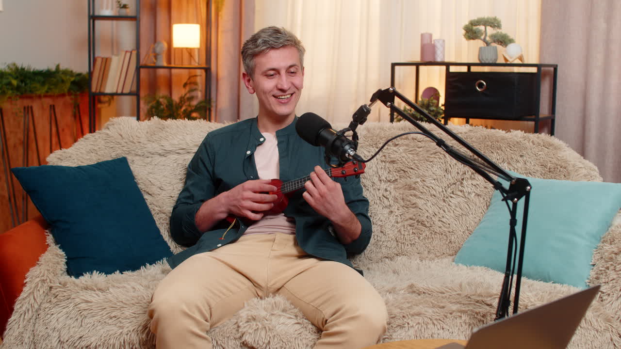 Young man joyfully plays toy ukulele recording fun music and singing in microphone with creativity