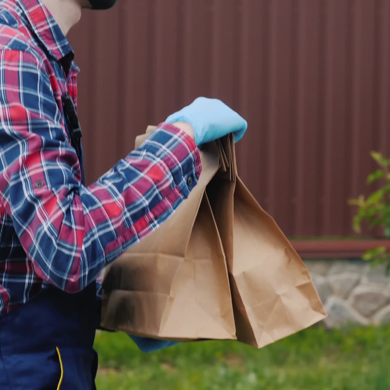 vista lateral de un hombre con una máscara y guantes que lleva bolsas de comestibles a la casa del cliente