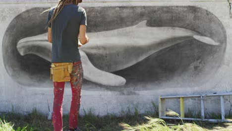 video of rear view of caucasian male artist with dreadlocks painting whale mural on wall