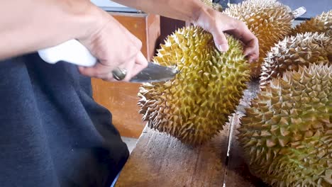 Street-seller-splitting-durian-fruit-with-sharp-knife-in-Indonesia,-close-up-view