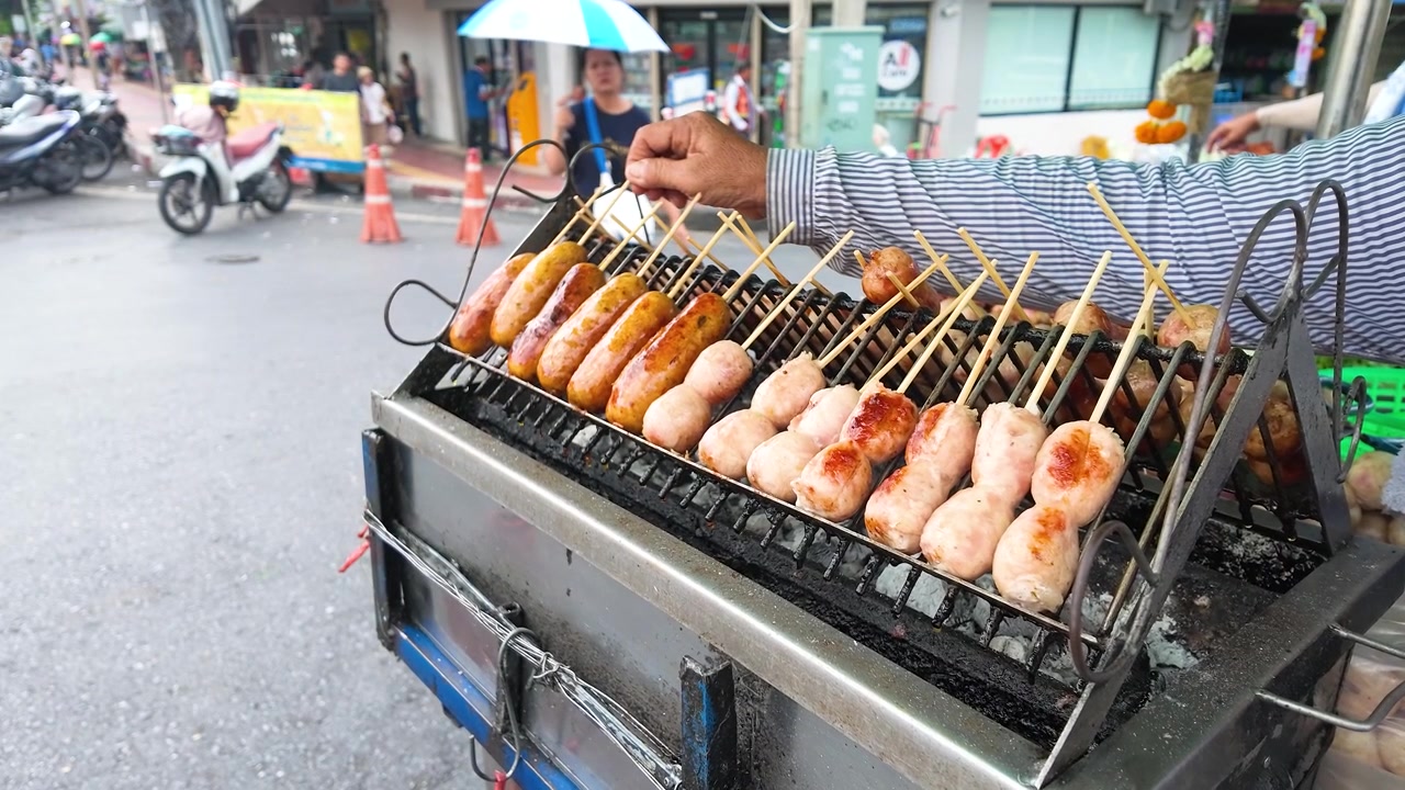 Seorang penjual membalik sate daging di atas panggangan arang di pasar jalanan Bangkok yang ramai.