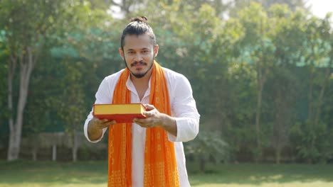 cute indian man offering sweet box to the camera