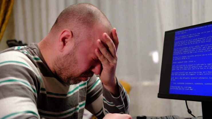 Ein Mann weint vor einem blauen Computerbildschirm. Zusammenbruch, Virus im Computer. Burnout, Erschöpfung als Konzept.