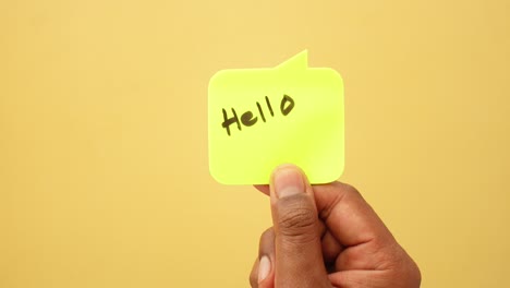 hand holding a yellow sticky note with the word hello written on it