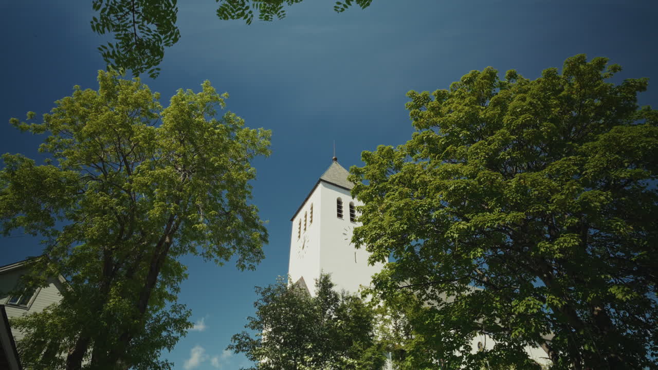 Panoramic view of a white local church surrounded by green tall trees in Tromso, Norway.