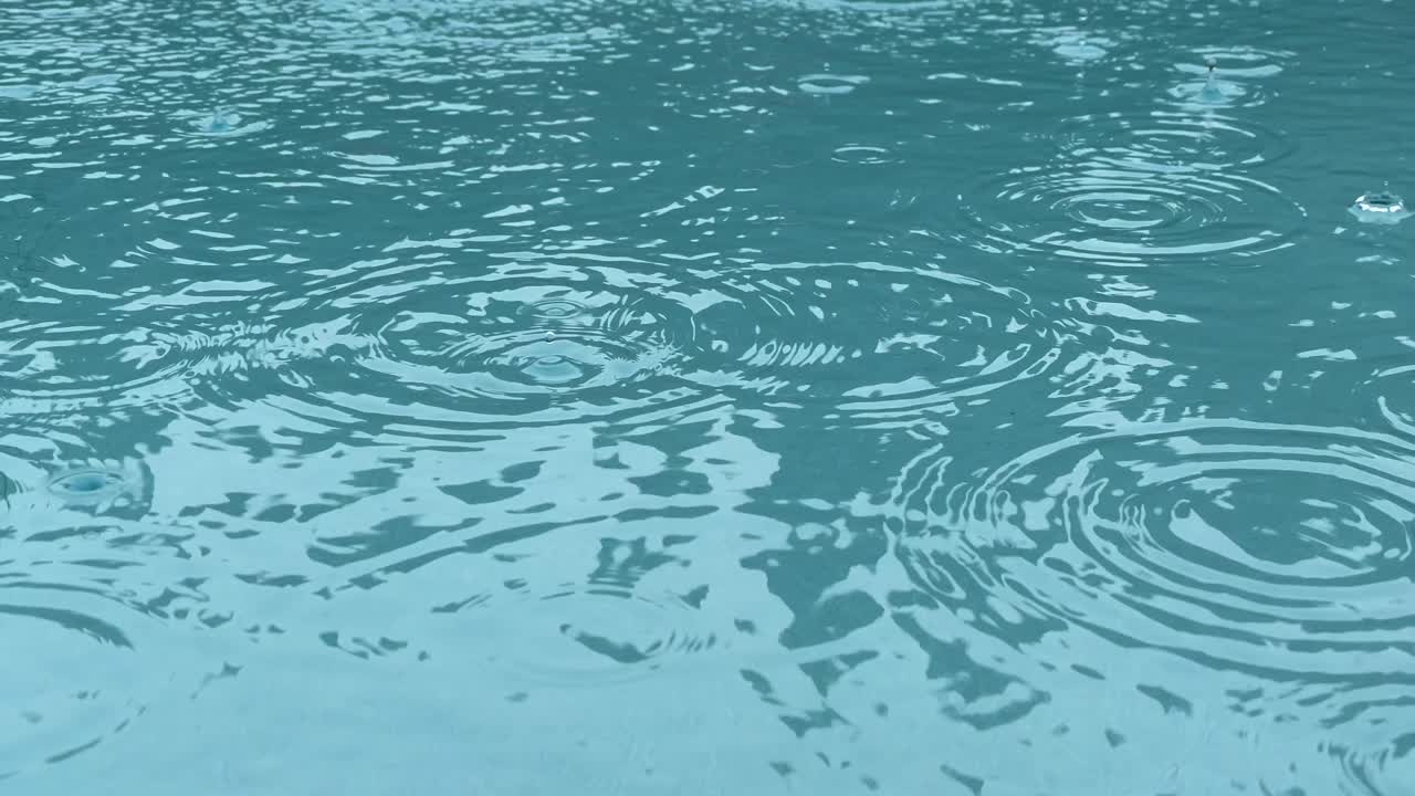Rain drops splashing into clean pool of aquamarine water, close up slow motion