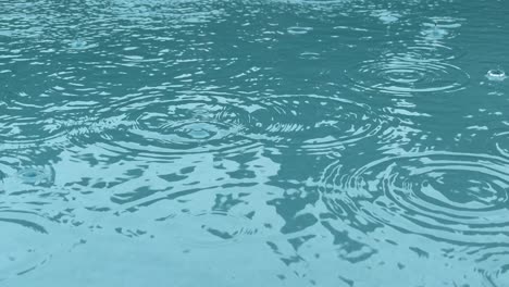 rain drops splashing into clean pool of aquamarine water, close up slow motion