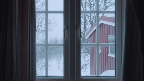 cozy view from a norwegian cabin window, capturing a serene winter forest scene with gently falling snow and charming red cabins nestled among snow-covered trees