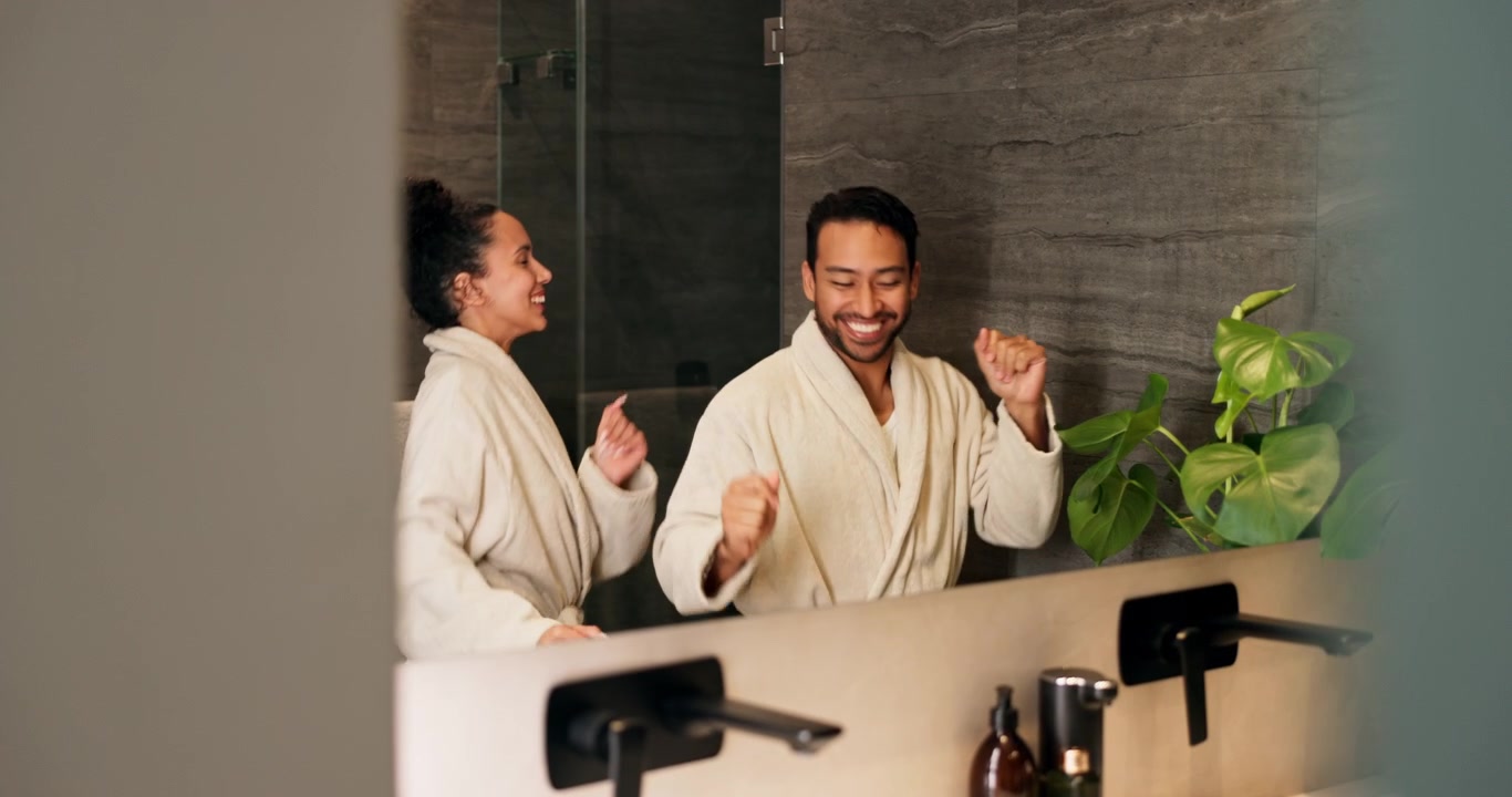Happy Couple Dancing Together in Bathrobes in Front of Bathroom Mirror