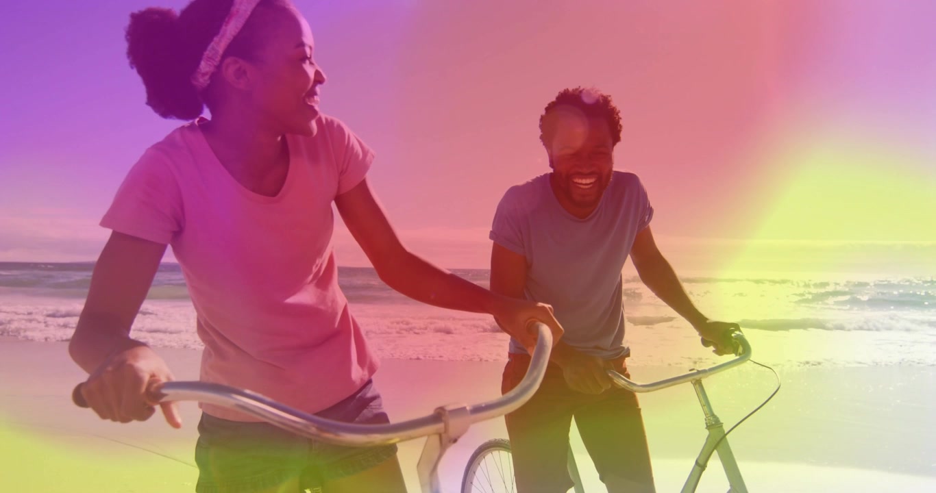 Travel couple walking beach with bikes woman talking sparking lightleak camera tightening laughing