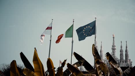 england, italian, and european flag fluttering in the wind with the famous duomo di milano in milan, italy