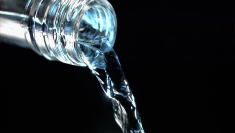 super slow-motion water trickles from a glass bottleneck with blue reflection on black.